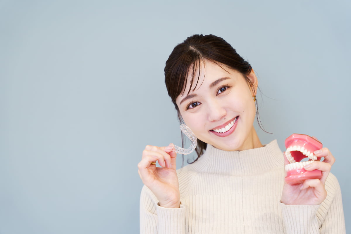 マウスピースと歯の模型を手に笑顔を見せる女性