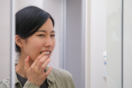 鏡を見て歯並びを気にする女性